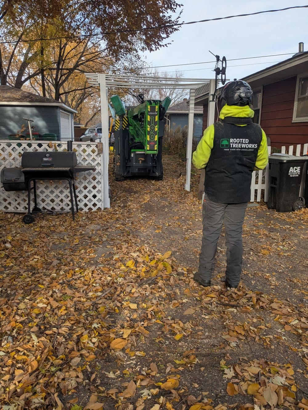 Tree service technician operating a wood chipper in a leaf-covered backyard.
