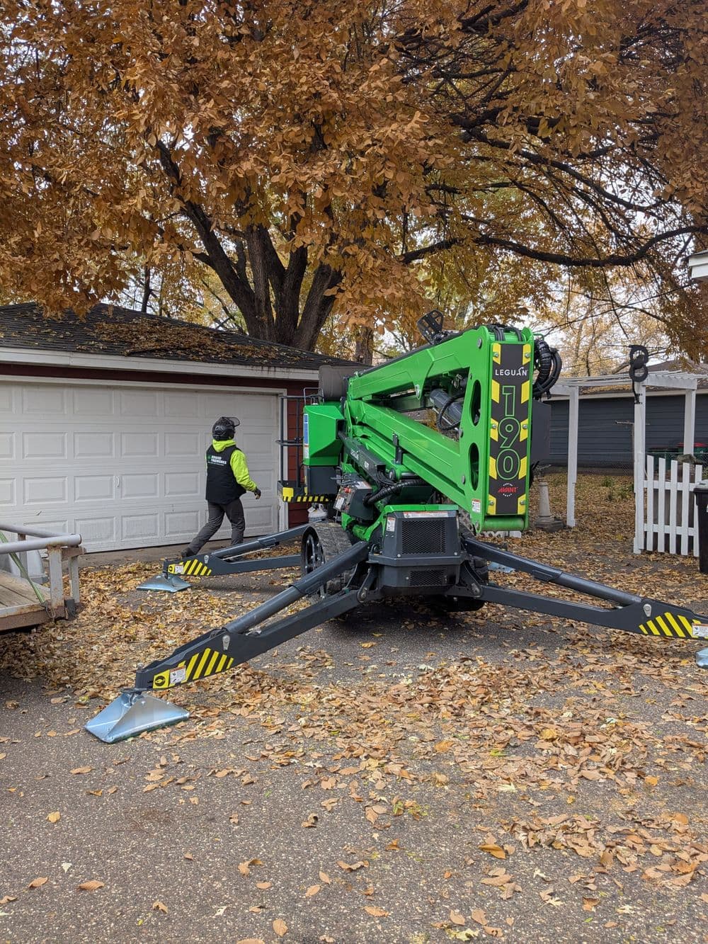 Tree trimming equipment parked near a garage, with a worker in a safety jacket nearby.