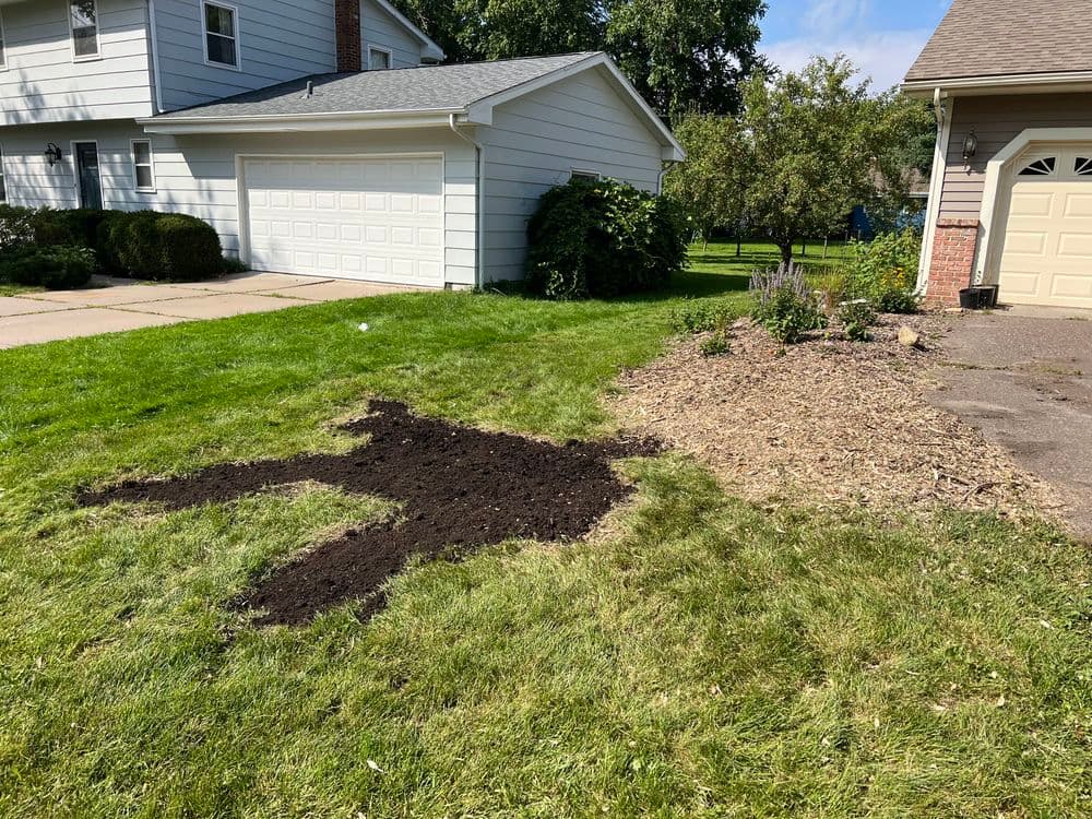 Unfinished landscaping project with a dirt patch and mulch area in a residential yard.