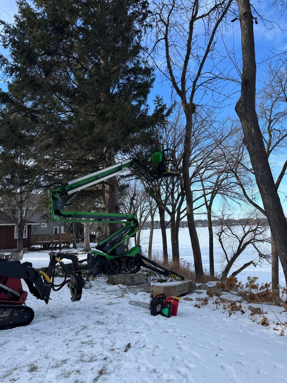 Skyline in winter with a green cherry picker tree trimmer near a frozen lake.
